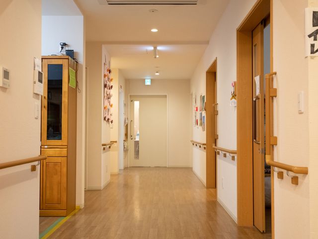 廊下の明るい空間 廊下 壁に飾られたアートが心地よいアクセントを加える廊下です。手すりが安全な歩行をサポートし、落ち着いた色合いの木目調が温かみを与えています。