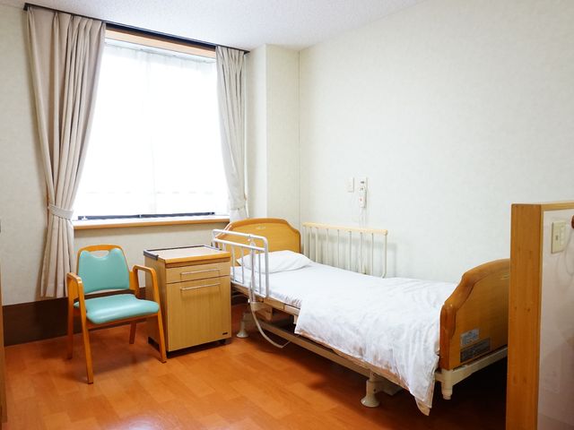 居室と窓 居室 ゆったりとしたベッドと温かみのある色合いの家具が配置された居室です。日差しが差し込む窓際には、ご自宅のような安らぎを感じられる椅子があります。