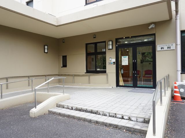 清潔な建物のエントランス 外観 スロープ付きのエントランスはバリアフリー設計で、明るい待合室が見えます。安全で快適な出勤が期待できる職場環境です。