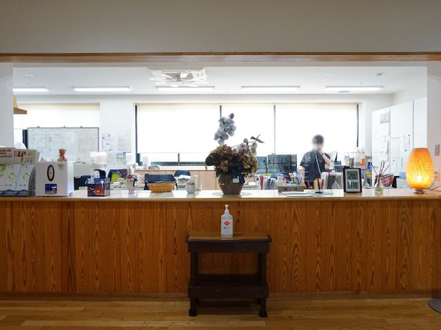 フロントカウンター設備 受付 暖かい灯りと木目調のカウンターが、訪れる人を温かく迎え入れています。スタッフの方々が活気に満ちた表情で業務にあたっており、快適な職場環境がうかがえます。