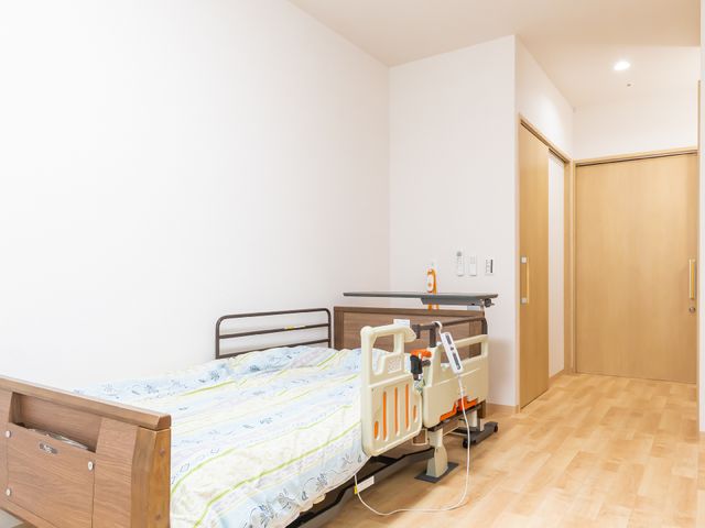 居室の明るい空間 居室 床の木目とベッドが調和して、温かみのある居心地の良い個室です。ゆったりとした時間を過ごすための落ち着いた環境が整っています。