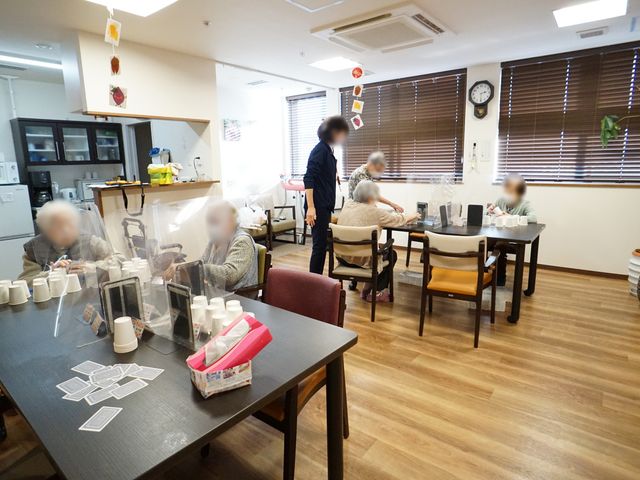 共有ダイニングエリア 共有スペース 落ち着いた雰囲気のダイニングルームで、利用者の方がテーブルを囲みながら食事の時間を楽しんでいます。スタッフが丁寧に対応しており、安心して日々を過ごせる様子がうかがえます。
