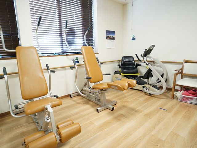 リハビリ用器具が並ぶ部屋 機能訓練室 健康維持のための機能訓練器具が整備された明るい環境です。如何なる方も安心してトレーニングに取り組めます。