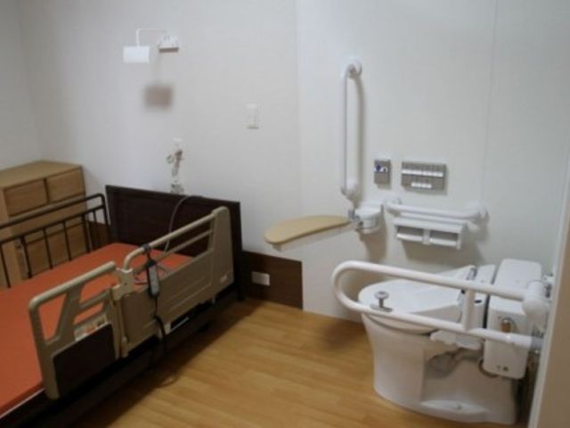 ゆったりとした居室 居室 手すりや広々とした洗面台が付いた室内は、安心して生活できる工夫が施されています。ベッド周りも清潔感があり、落ち着いた色合いでまとめられています。
