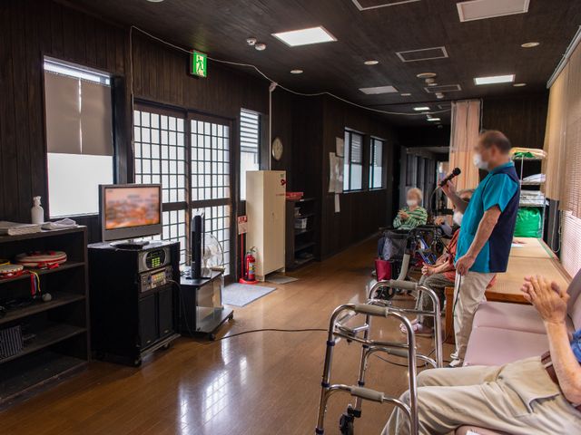 多機能スペース利用シーン 共有スペース ゆったりとした空間の多目的室で、居住者がカラオケを楽しんでいます。明るく暖かみのある雰囲気が、日々の活動に彩りを加えます。