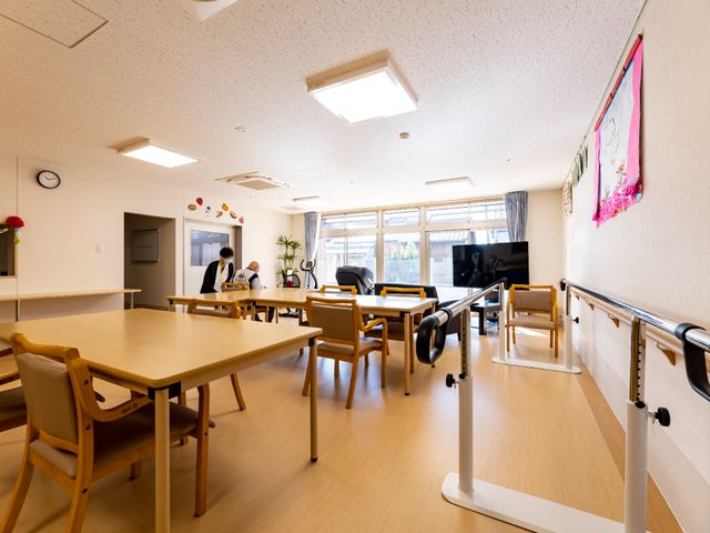 共用ダイニングスペース 多目的室 天井が高く開放感のあるダイニングスペースで、職員と利用者様がテーブルを囲み会話を楽しんでいます。집-