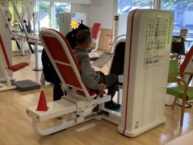 トレーニング機器と利用者 デイサービス 明るく清潔な空間で、利用者が機能訓練を行っています。充実した設備のもと、ご自身のペースで体力維持に取り組めます。