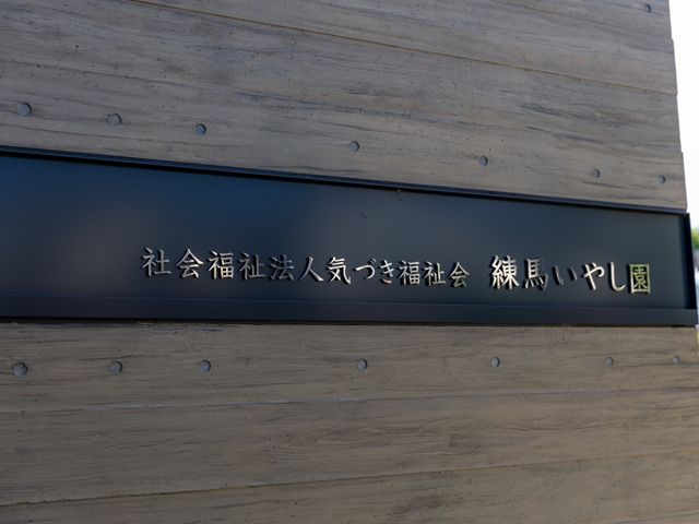 施設名看板の外観 看板   木目調の壁に黒い看板が映える外観です。施設名が見やすく、落ち着いた雰囲気が伝わります。