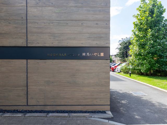 施設名のある外観 外観   木目調の外壁と緑が印象的な外観です。落ち着いた雰囲気で、働く場所としても親しみやすく感じられます。