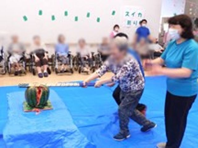 レクリエーション活動 多目的室 利用者とスタッフがスイカ割りを楽しむ活動風景です。みんなで楽しい時間を過ごしています。