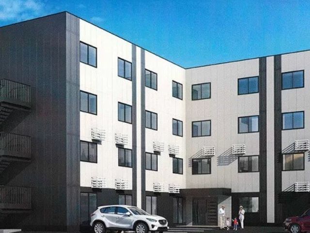 白と黒のモダンな外観 現代的なデザインの建物です。広々とした駐車場があり、入口付近には来訪者を迎えるスタッフの姿も見えます。