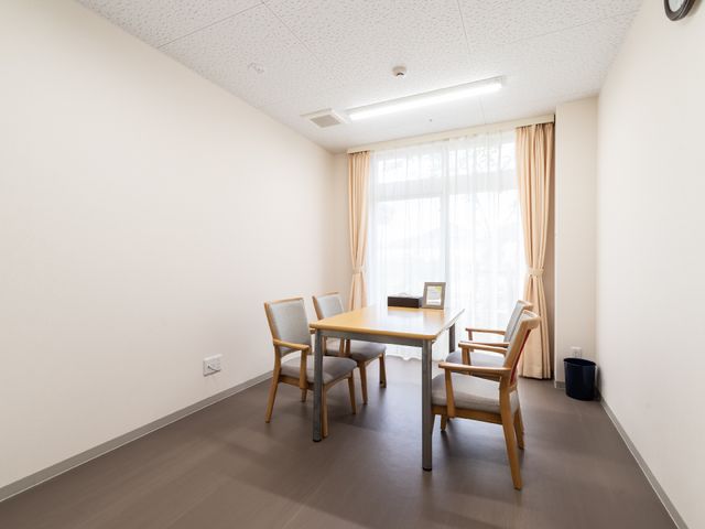 居室のシンプルな空間 共有スペース 落ち着いた雰囲気の居室です。机と椅子が配置され、窓からは自然光が差し込んでいます。