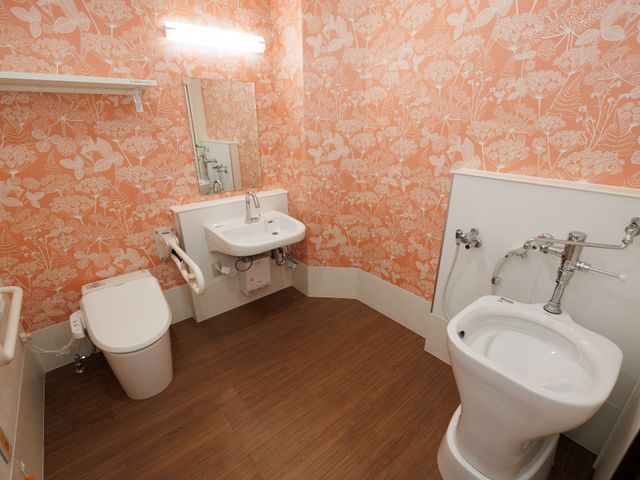 明るい配色の洗面所 トイレ サポートバー付きのバリアフリー対応トイレです。安全かつ快適に利用できる設計で、利用者の自立した生活を支援します。