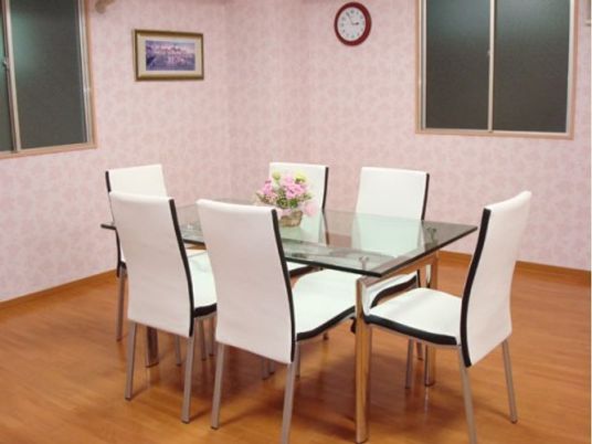 施設の写真 ピンクの壁紙が特徴的な明るいダイニングである。天板がガラス製の６人掛けダイニングテーブルが置かれている。