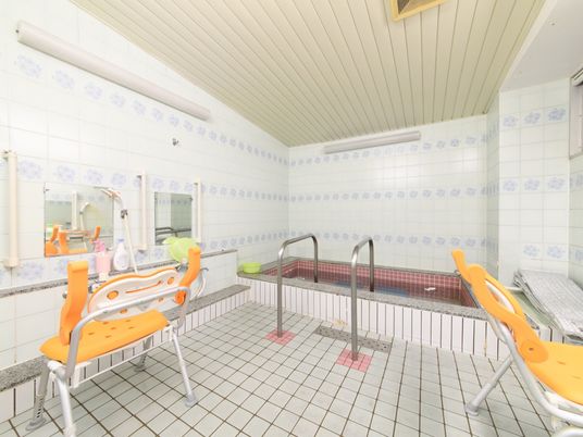 施設の写真 ほぼ全面がタイル張りで、複数のカランが設置されている浴室である。台の上にはシャンプーなどを置けるスペースがある。