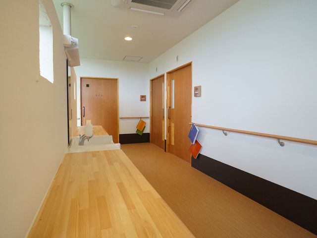 手すり付きの明るい廊下 廊下A ゆったりとした温かみのある木目調の廊下が、職場での快適な移動をサポートします。壁沿いに取り付けられた手すりが、歩行の安全を考慮しています。