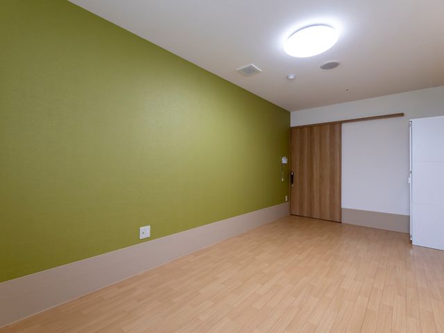 空間広々とした居室 居室 清潔感溢れる明るい居室が広がっており、心地よいプライベート空間を提供しています。壁と床の色合いが落ち着いた雰囲気を醸し出し、穏やかな毎日を過ごせると感じられます。