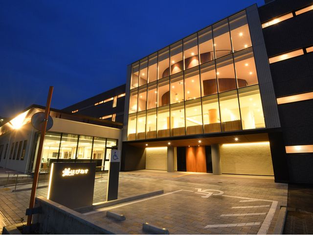 夕暮れ時の施設外観 外観 落ち着いた色調の外観は、夕暮れに温かみを放ち、歓迎する雰囲気を醸し出しています。夜間も明るく照らされ、安心感を与える設計になっております。