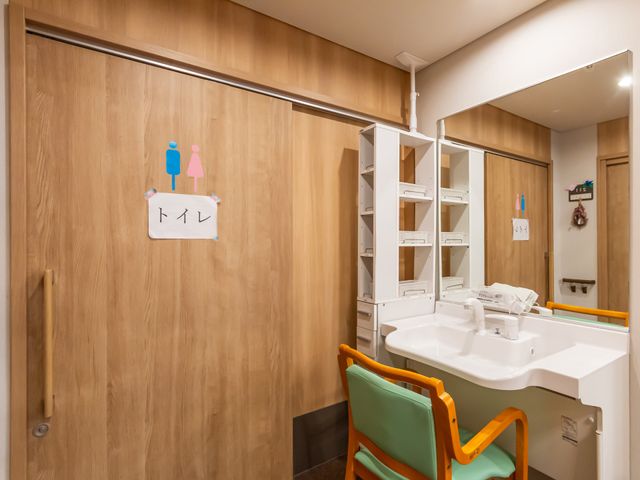 洗面台と扉の前 トイレ 広々とした洗面台が設置されており、木目調の扉が落ち着いた雰囲気を演出しています。
