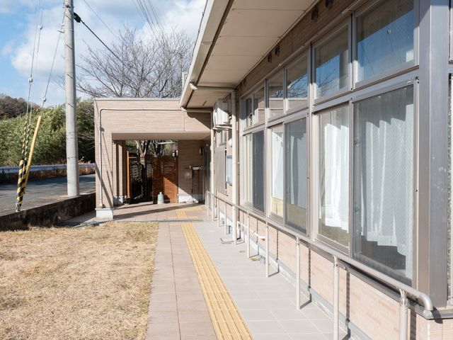 晴れた日の施設の外観 玄関 日差しに包まれた清潔感のある入口がお迎えします。安心して新しい生活を始められる環境が整っています。