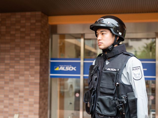 警備員が施設前に立つ セキュリティ 施設の安全を守る警備員の姿です。安心してお仕事に専念いただける環境が整っています。