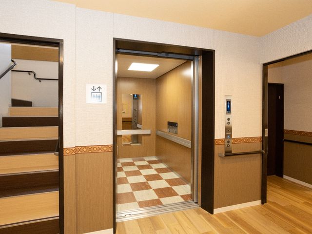 廊下とエレベーター エレベーター 手すりが設置されている廊下は安全でナチュラルなデザインです。皆様の快適な移動をサポートいたします。