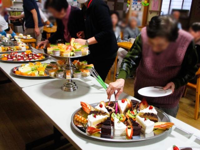 色とりどりのケーキが並ぶテーブル ダイニングルーム 色とりどりのケーキが並べられたテーブルで、利用者同士が和やかに会話を楽しんでいます。