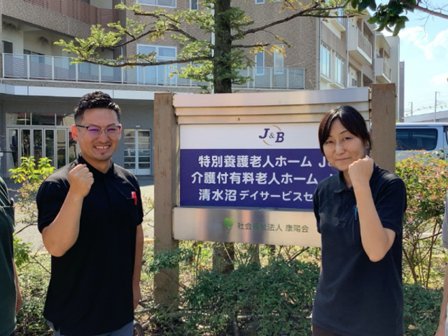 エントランス前の看板 看板 施設の前でスタッフが元気な姿勢を見せています。明るく前向きな職場環境が感じられます。