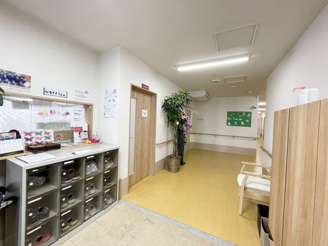 明るく清潔なエントランス 玄関 手すりが付いた廊下と、ゆったりとしたスペースのある待合室の光景です。スタッフや訪問者のコミュニケーションも取りやすい設計になっています。