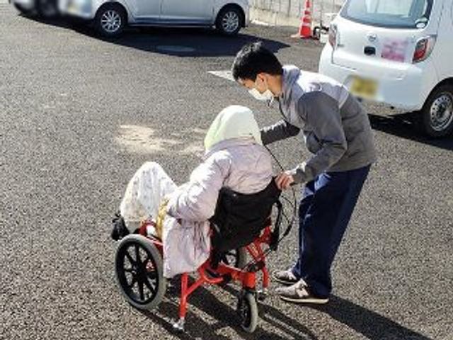 車椅子介助の駐車場 スタッフイメージ 車椅子の方がスタッフに付き添われています。温かみのあるサポートが印象的です。