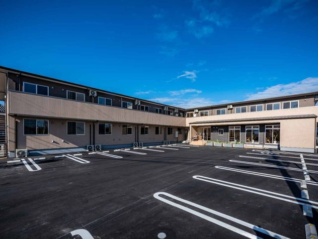 明るい日差しの中の外観 外観 広々とした駐車スペースを備え、青空のもとに佇むモダンな建物です。興味をお持ちの方はぜひ一度足を運んでみてください。