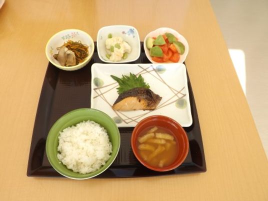 正方形のトレーに並べられた１食分の食事。メインの魚料理とご飯と汁物の他に、３品の副菜が置かれている。