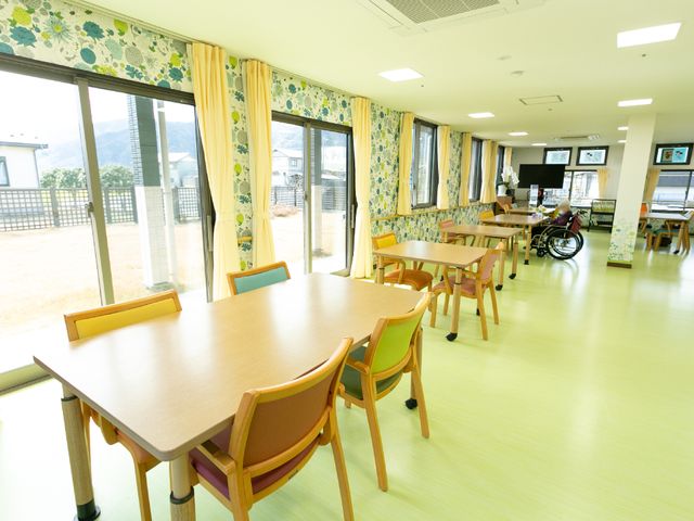 日当たりの良い広々とした食堂 共有スペース ゆとりあるレイアウトの食堂では、大きな窓から光が差し込み、車いすをご利用の方がいらっしゃいます。明るく開放感のあるこの空間で、快適なお食事の時間を過ごせそうです。