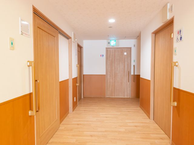 清潔感ある廊下の様子 廊下 木目調の扉と手すりが暖かみのある廊下は、足元にも配慮したバリアフリー設計です。スタッフと利用者の円滑な移動に配慮された空間が広がっています。