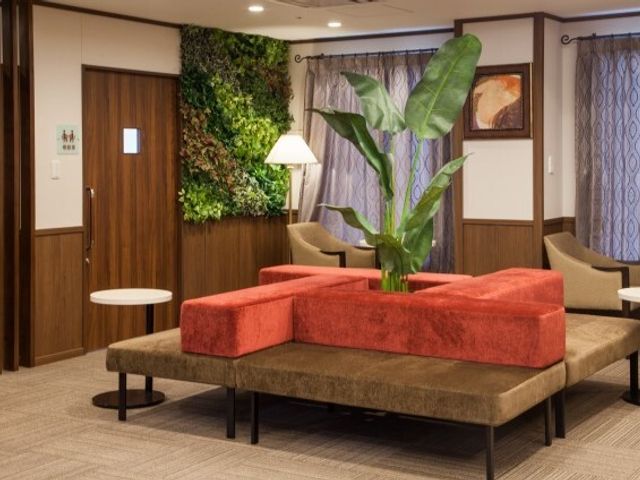 植物飾る応接スペース エントランス ゆったりとした赤いソファが置かれたラウンジでは、訪れる方々が心地よい時間を過ごすことができます。自然の緑が癒しの空間を演出しています。