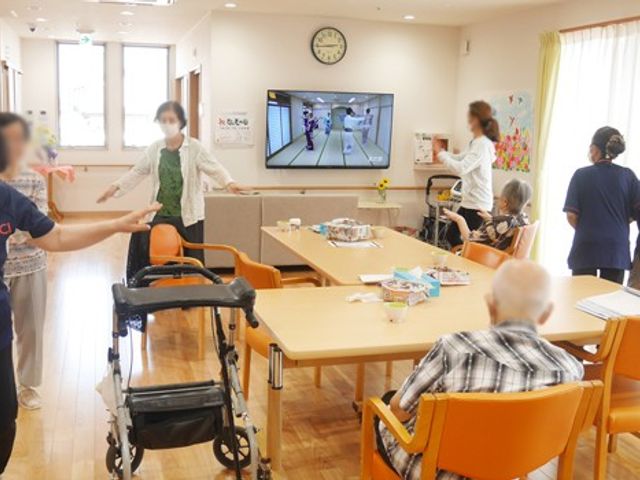 リビングの様子 リビング 自然光が溢れるリビングで、入居者の方々が体操を楽しんでいます。広々とした空間が魅力です。