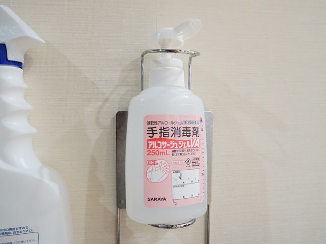 壁に取り付けられた消毒液 アルコール消毒液 手指の衛生を確保するため、廊下には消毒液の設置があります。安心して日々の業務に臨める環境が整っています。