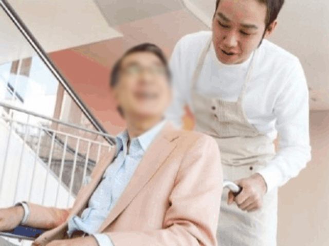 職員と利用者の様子 廊下 職員が利用者をサポートしながら、明るいスペースを移動しています。安心して働ける環境です。