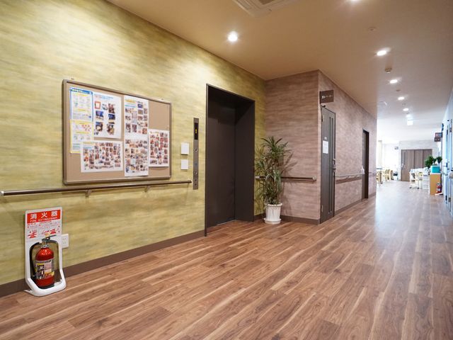 廊下と掲示物 廊下 明るく広々とした廊下は、木目調の床で落ち着いた雰囲気を醸し出しております。壁面の掲示板には、日々の活動や情報が丁寧に掲示されています。