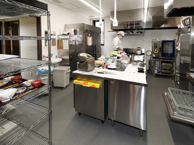 清潔なキッチン作業風景 厨房 厨房の設備が整った清潔な作業スペースで、調理員が作業に取り組んでいます。こちらで新鮮な食材を使って、栄養満点の食事の提供を行います。