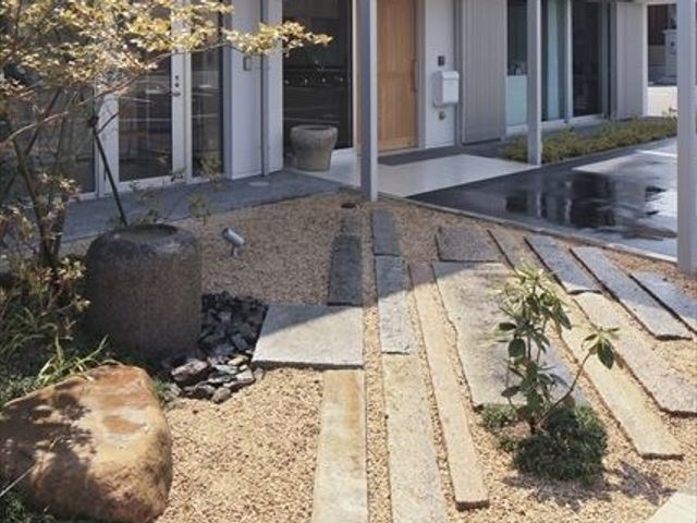 庭園風の外回り 庭   砂利と石材を使った落ち着いた外回りです。植栽があり、建物の出入り口へ続く通路が見えます。