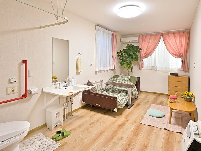 明るい居室の一角です 居室   木目の床とやわらかなカーテンが印象的な居室です。洗面台やベッド周りが整っており、落ち着いて過ごしやすそうです。