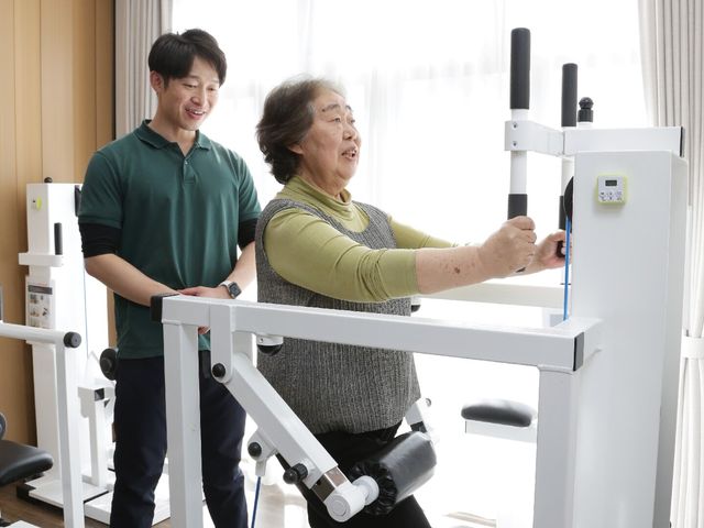 運動支援の瞬間 リハビリ 笑顔で支援するスタッフと共に、元気にトレーニングをこなす様子が見て取れます。働く側もやりがいを感じられる空間です。