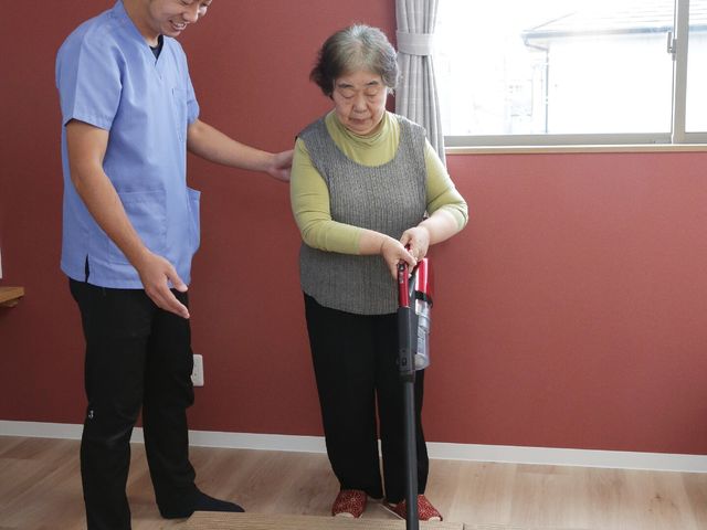 支援と共に掃除をする様子 リハビリ ケアスタッフが見守る中、清掃作業を行う利用者の姿です。日常生活の一部として、機能訓練も積極的に取り入れられています。