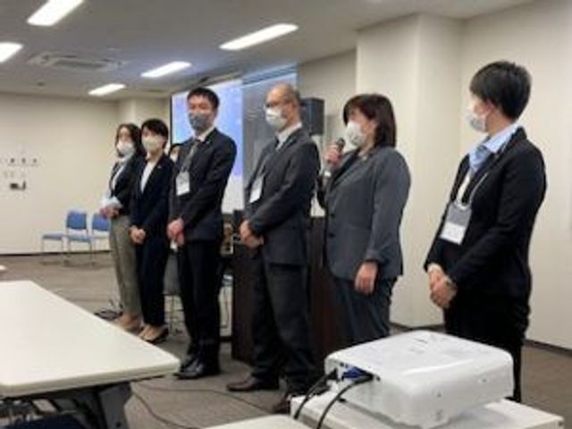 スタッフが並ぶ会議室 多目的室   スタッフの方々が並んで立つ、広めの多目的室です。明るい照明が入った落ち着いた空間で、打ち合わせにも使いやすそうです。