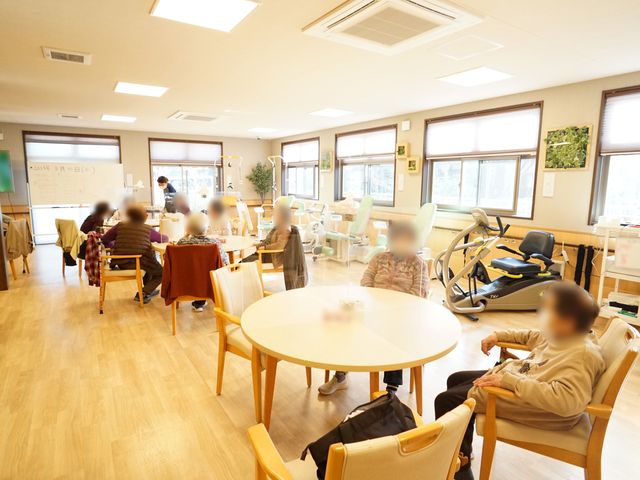 機能訓練の様子が見える部屋 共有スペース 明るく広々とした空間で、リハビリマシンを使った機能訓練が行われています。利用者の方々がそれぞれのペースで、リラックスした雰囲気の中、過ごされています。
