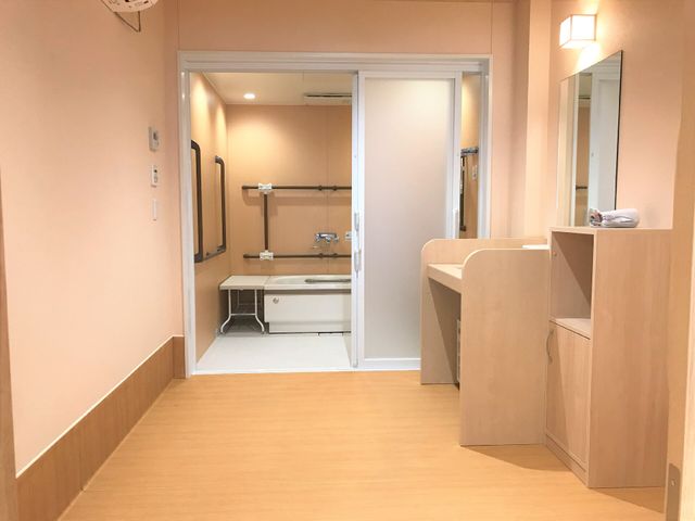 洗面台付きの明るい廊下 脱衣所 洗い場がすべりにくい材質で、安全に配慮されたバリアフリーな洗面スペースです。入居者の日々の快適さを重視した設計を感じます。