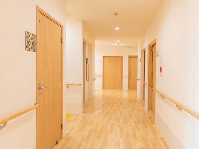 明るい木目調の廊下 廊下 手すり沿いに広がる通路は、明るく清潔感があります。仕事に就くごとに、ここを通る安心感を感じていただけるでしょう。