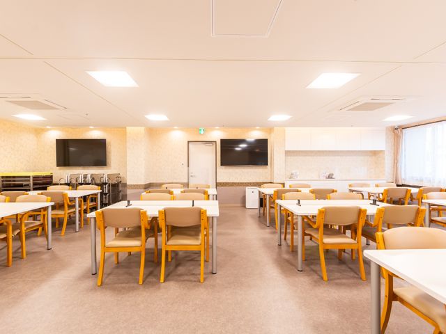 広々とした明るい食堂 共有スペース ゆったりしたテーブルと椅子が配置された食堂で、ゆとりをもってお食事や社交が楽しめます。壁には大画面のテレビがあり、共有スペースとしても機能しています。