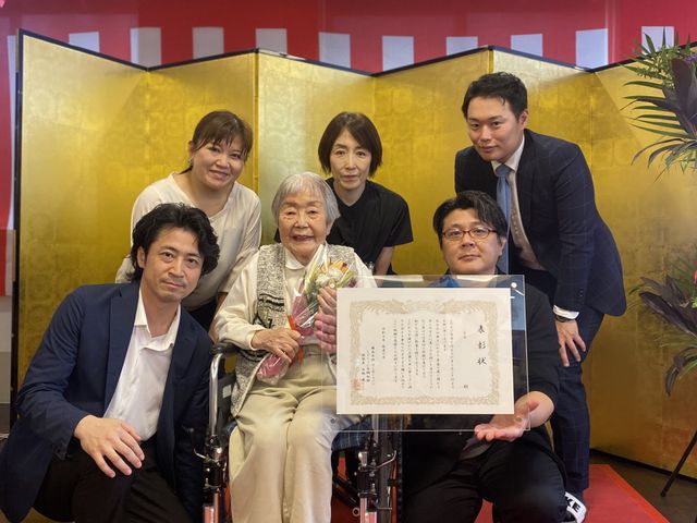 敬老会ポスターと人物 掲示物 笑顔で集合写真を撮っており、祝賀会の華やかさが伝わります。和やかな雰囲気での記念撮影です。